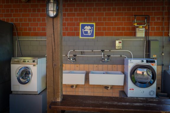 Waschplatz Zwei Waschmaschinen und zwei Waschbecken an einer Wand mit Ziegelsteinen.