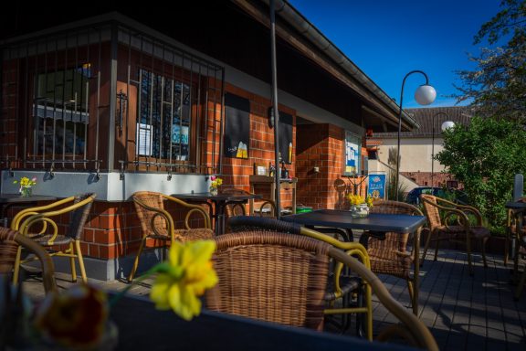 Kleine Pause - unsere Außenterasse Gemütliches Café mit Rattanmöbeln und bunten Blumen im Freien bei klarem Himmel.